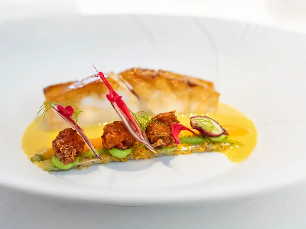 Gerecht van Restaurant GEM. met gebakken vis, kruidige garnituur en gele saus op een wit bord