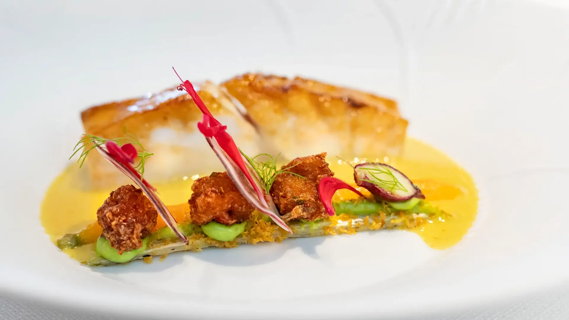 Gerecht van Restaurant GEM. met gebakken vis, kruidige garnituur en gele saus op een wit bord