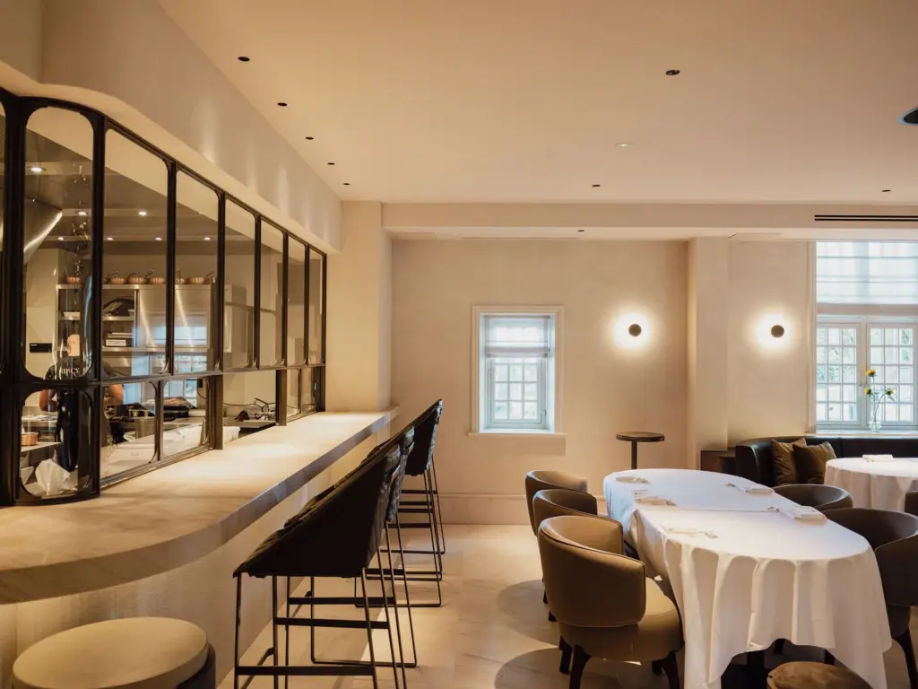 Restaurantzaal met een lange bar, een stalen glazen wand en gedekte tafels met wit tafellinnen