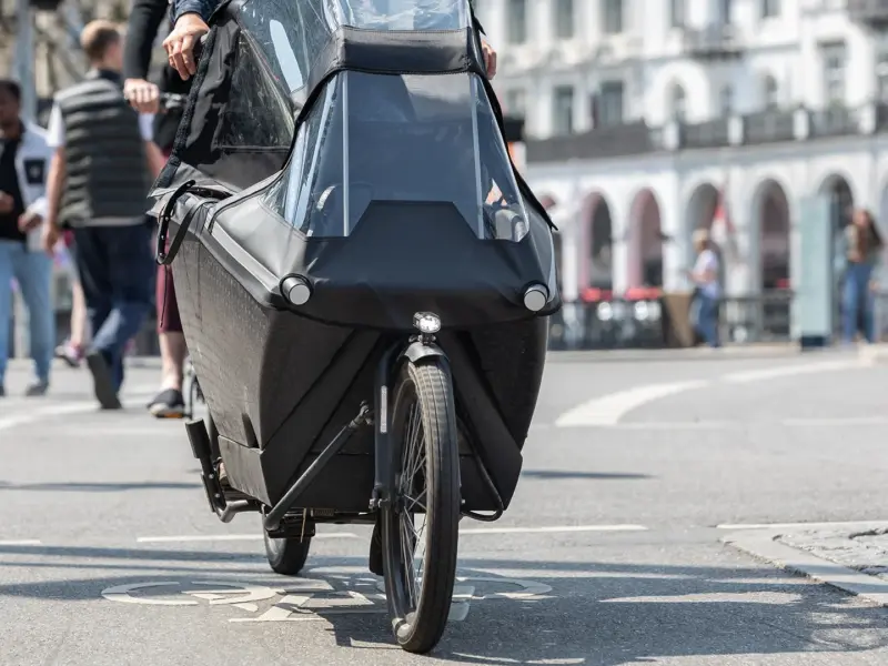 Zwarte bakfiets met regenkap op een fietspad in een stad