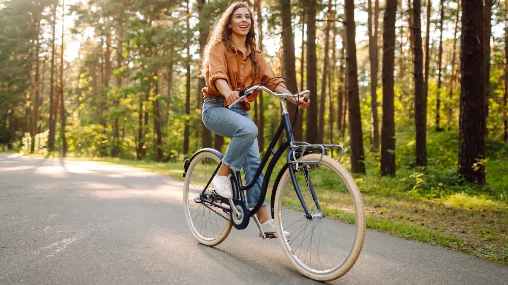Vrouw fietst op een stadsfiets over een bosweg in de zon