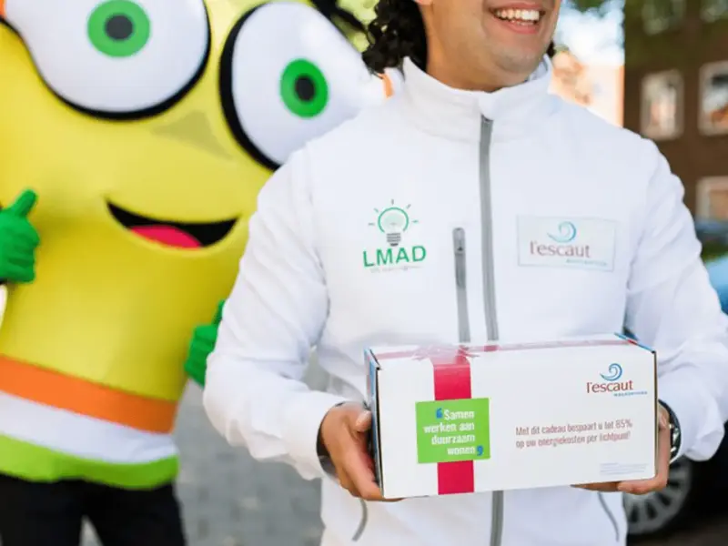 Mascotte Leddy en een medewerker van woonservice l'escaut met een cadeaubox voor de LMAD-actie "Samen werken aan duurzaam wonen"